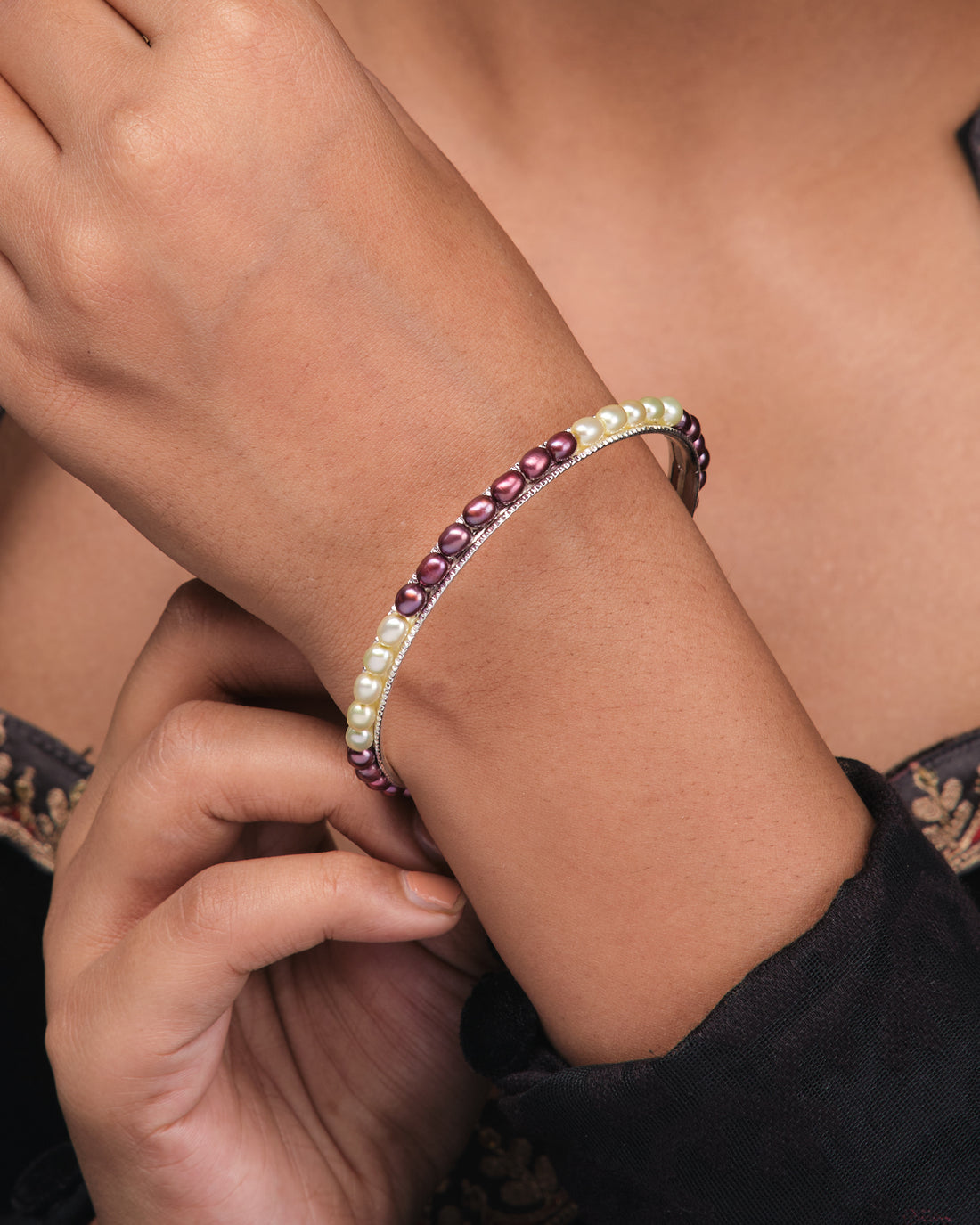 The Chandrani Pearls Single Line Black & White Bangle (B01731) stands upright on a pink surface, with a purple cloth in the background.