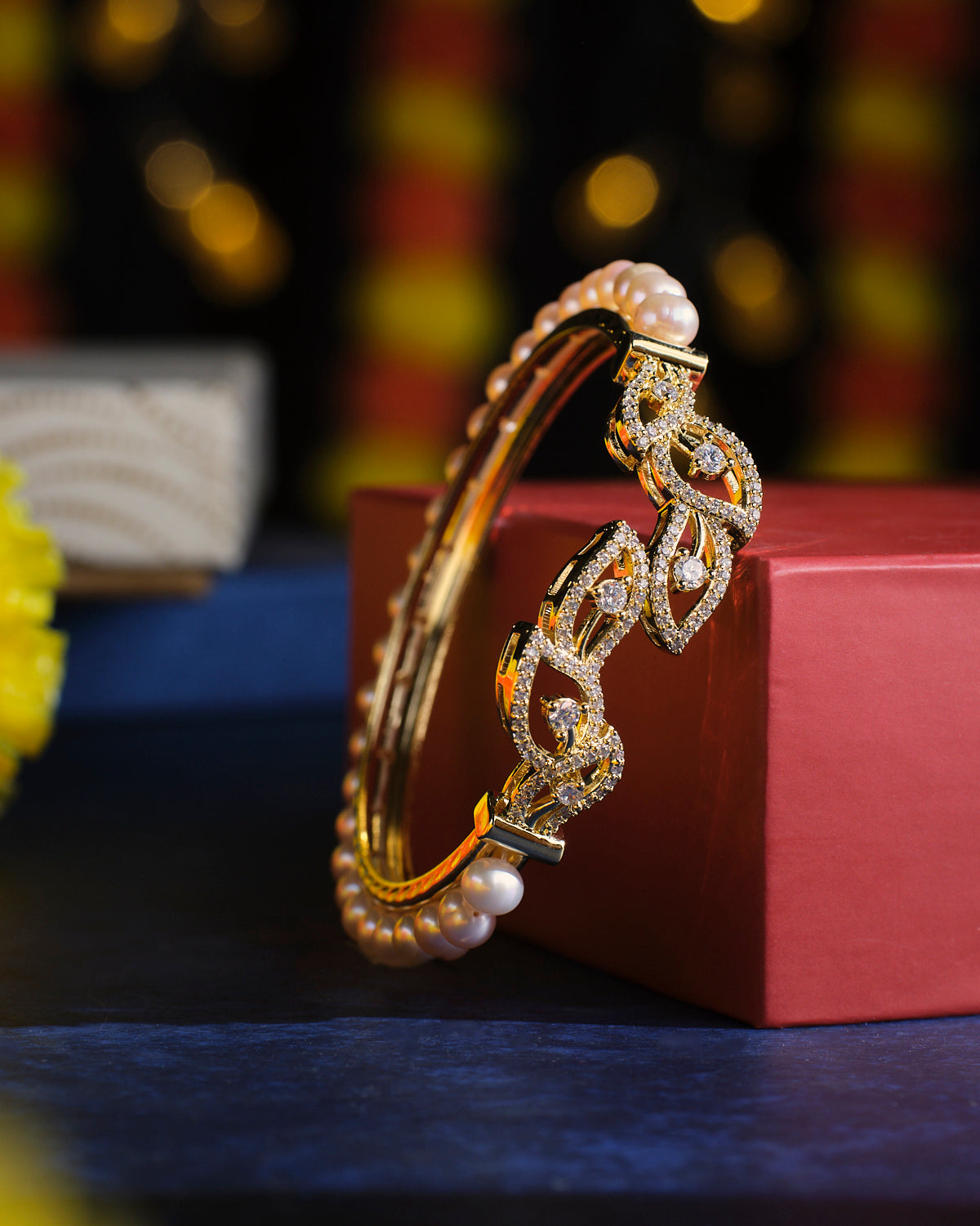 The Serene Leaves Pearl Bangle by Chandrani Pearls, featuring intricate designs, rests on a red box against a softly blurred background.