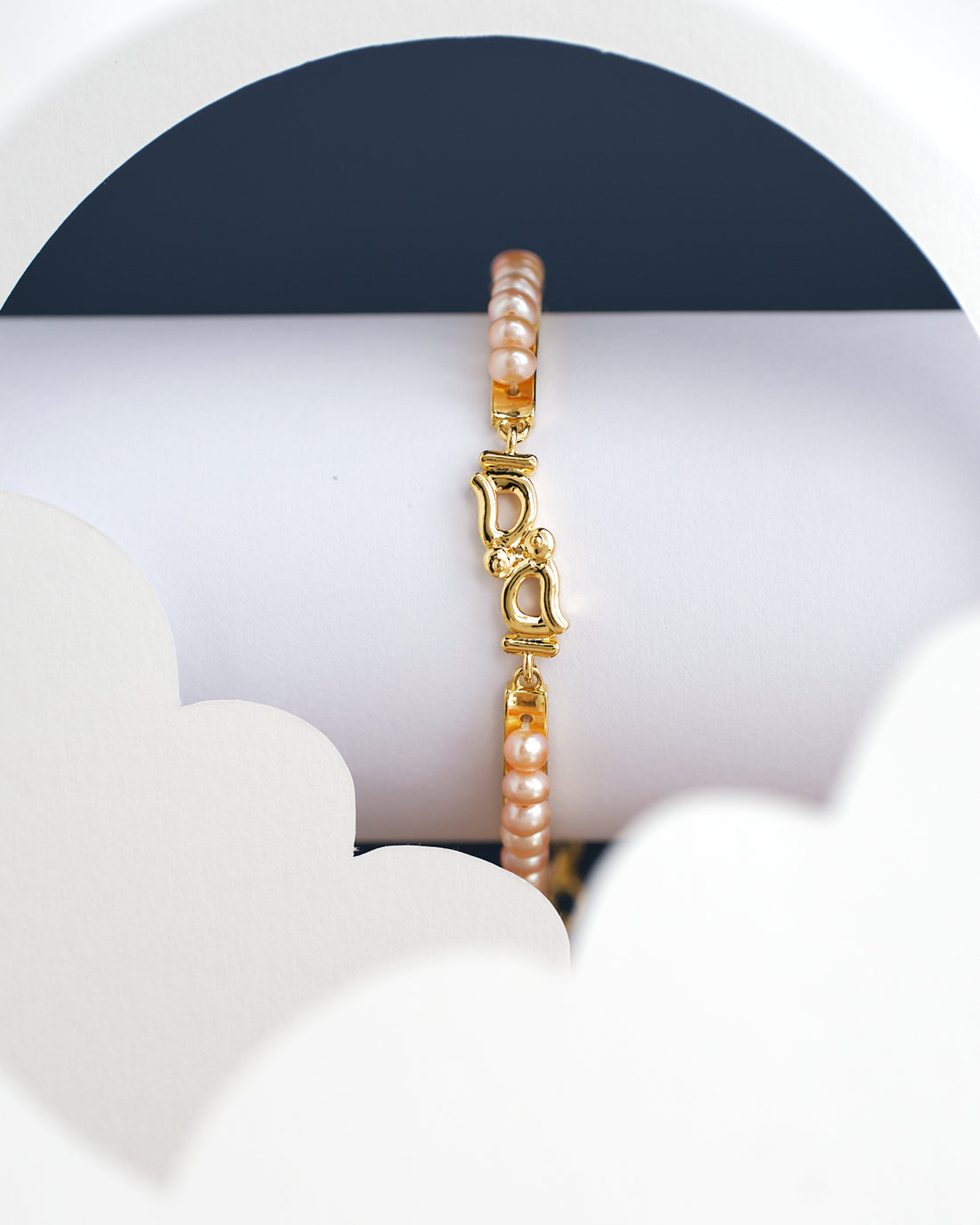 Kyra Pearl Bangle for kids by Chandrani Pearls India, featuring a gold bracelet with a "D" charm and pearl beads, displayed on a white geometric background.