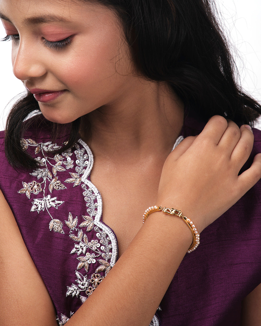 Kyra Pearl Bangle for kids by Chandrani Pearls India, featuring a gold bracelet with a "D" charm and pearl beads, displayed on a white geometric background.