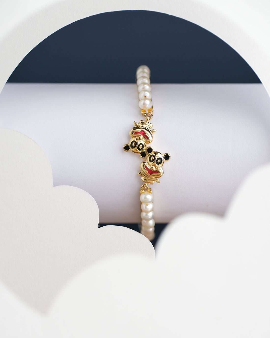 The Monkey Pearl Bangle for kids by Chandrani Pearls India, showcased with gold cartoon character charms, is set against a white and dark background with cloud-like cutouts.