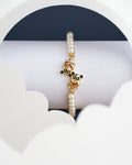 The Monkey Pearl Bangle for kids by Chandrani Pearls India, showcased with gold cartoon character charms, is set against a white and dark background with cloud-like cutouts.