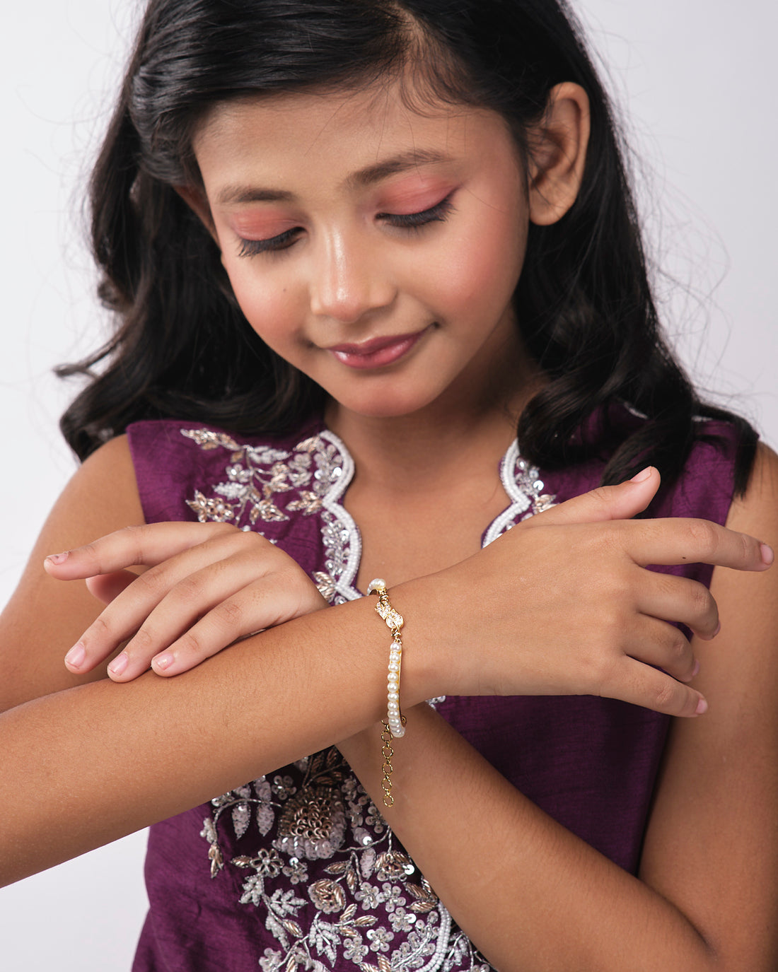 The Leafy Pearl Bangle for kids by Chandrani Pearls India, featuring a gold clasp, is showcased against a white and dark blue abstract background.