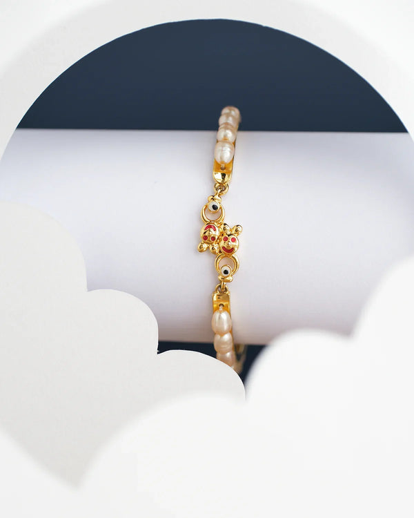The Teddy Pearl Bangle for kids by Chandrani Pearls India, featuring pearl beads and a butterfly design, is displayed on a white and navy blue background.