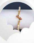 The Fishy Pearl Bangle for kids by Chandrani Pearls India, featuring gold with pearl accents and colorful bird ornaments, is displayed on a white and blue backdrop.