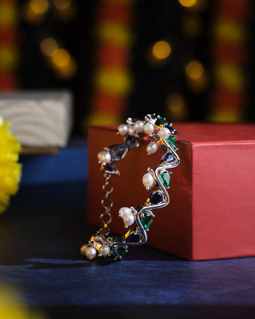 The Zigzag Cluster Pearl Bangle by Chandrani Pearls is elegantly displayed on a red box with a backdrop of softly glowing lights.