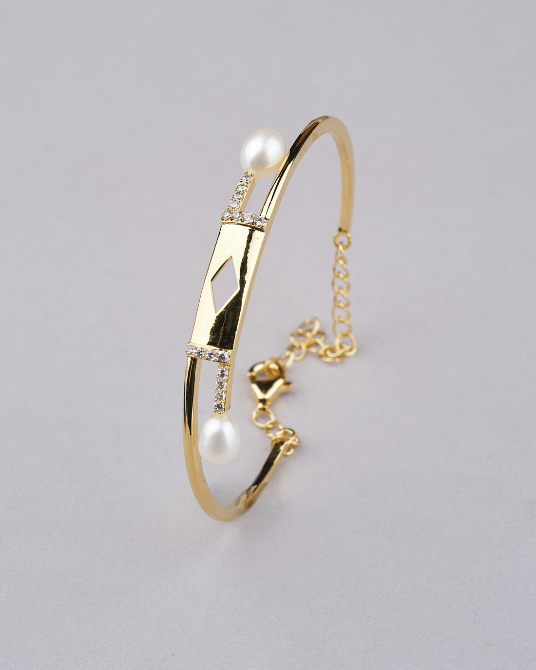 The Quad and Pearl 925 Silver Bangles by Chandrani Pearls India feature a geometric centerpiece, pearls, and a chain clasp, elegantly displayed on a red surface beside a red rose.