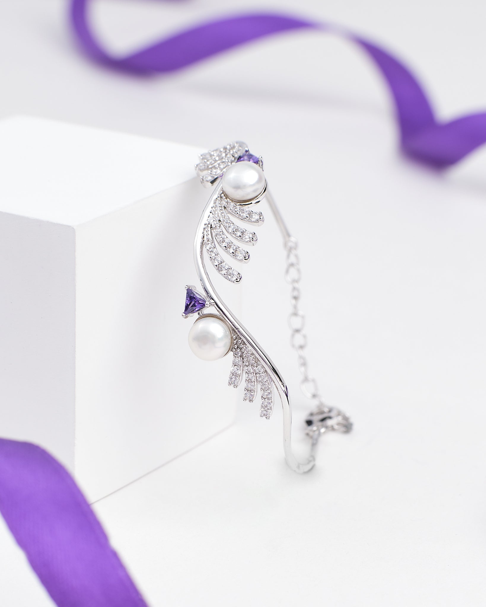 The Chandrani Pearls Luxury Tennis Bracelet in Sterling Silver with CZ Stones is showcased on a white block, accented by a purple ribbon in the background.