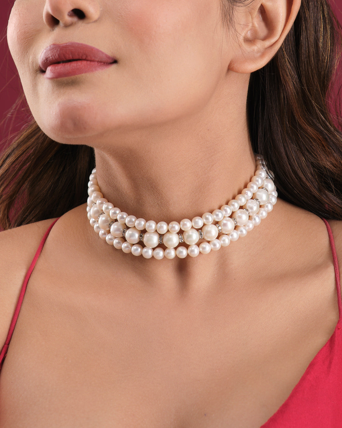 The Elegant Triple Line Choker by Chandrani Pearls India showcases refined glamour on a white jewelry stand, set against a softly blurred floral backdrop.