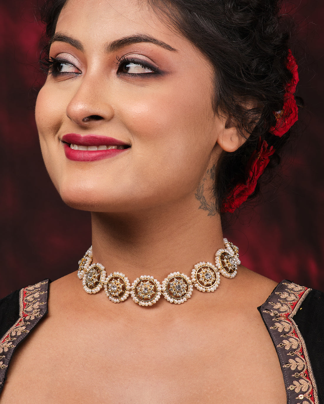 The Kanakshobha-Golden Grace Traditional Pearl Choker by Chandrani Pearls is shown on a black mannequin with draped dark red fabric and background—a timeless, elegant accessory for classic style.