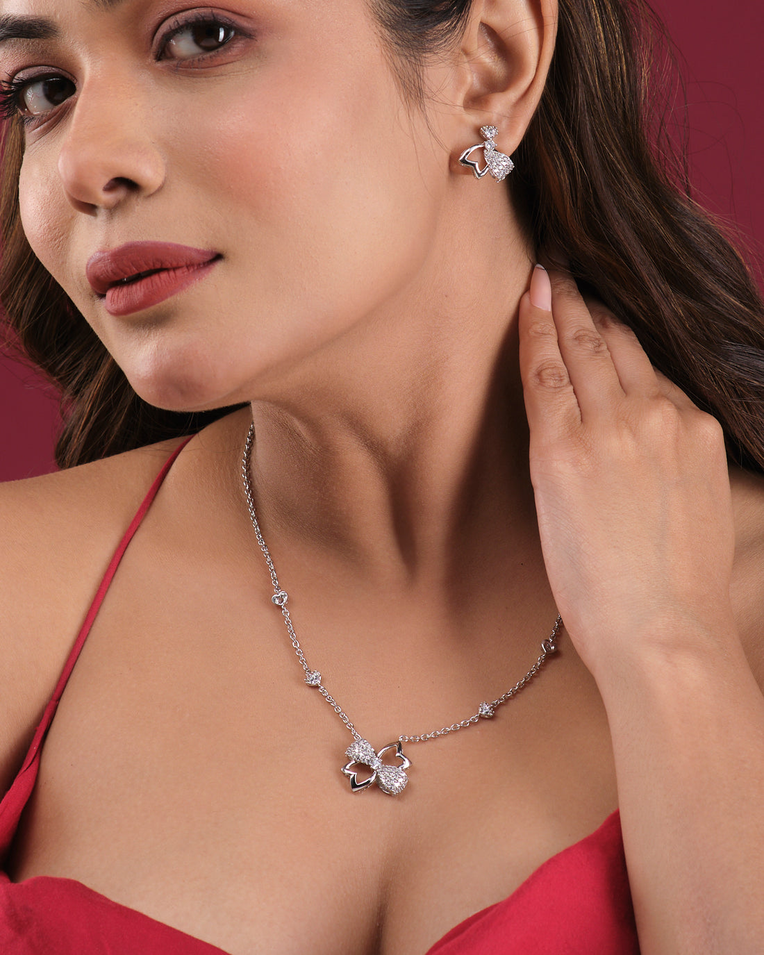 The Cute Pendant Set by Chandrani Pearls India, featuring a necklace and matching butterfly-shaped earrings displayed on stands, radiates graceful elegance against contrasting backgrounds.