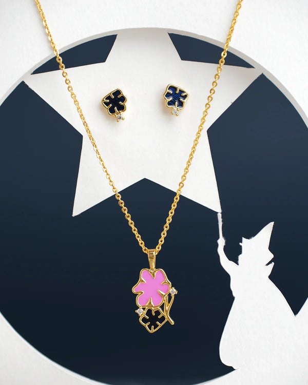 The Floral Enamel Pendant Sets by Chandrani Pearls India include a gold necklace with a pink flower and black clover pendant, paired with black clover stud earrings, displayed against a wizard silhouette and star background.