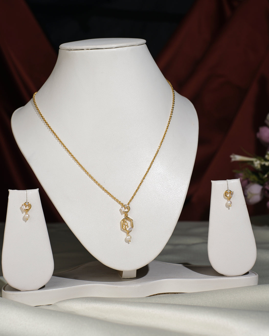 The Simple Pendant Set by Chandrani Pearls India features geometric shapes and small pearl accents, displayed on a white stand against a dark background; chain shown is for photographic purposes only.