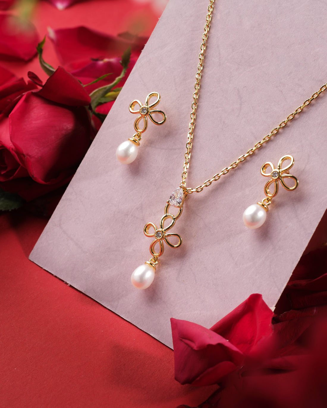 The Pretty Petals 925 Silver Pendant Set by Chandrani Pearls India features a floral design with pearl drops and matching earrings, beautifully displayed on a card with red rose petals—ideal for any special occasion.