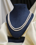 The Classic Single-Strand Pearl Necklace by Chandrani Pearls is displayed on a navy blue velvet bust, with cream-colored fabric draped in the background.