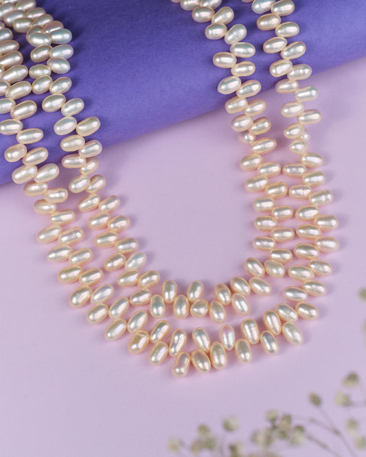 The Lavish Layers Of Elegance Pearl Necklace by Chandrani Pearls exudes sophistication as it rests gracefully on a light purple surface, with a deeper purple roll enhancing the background.