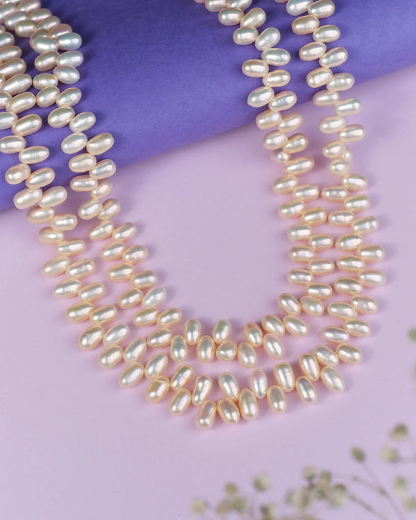 The Lavish Layers Of Elegance Pearl Necklace by Chandrani Pearls exudes sophistication as it rests gracefully on a light purple surface, with a deeper purple roll enhancing the background.