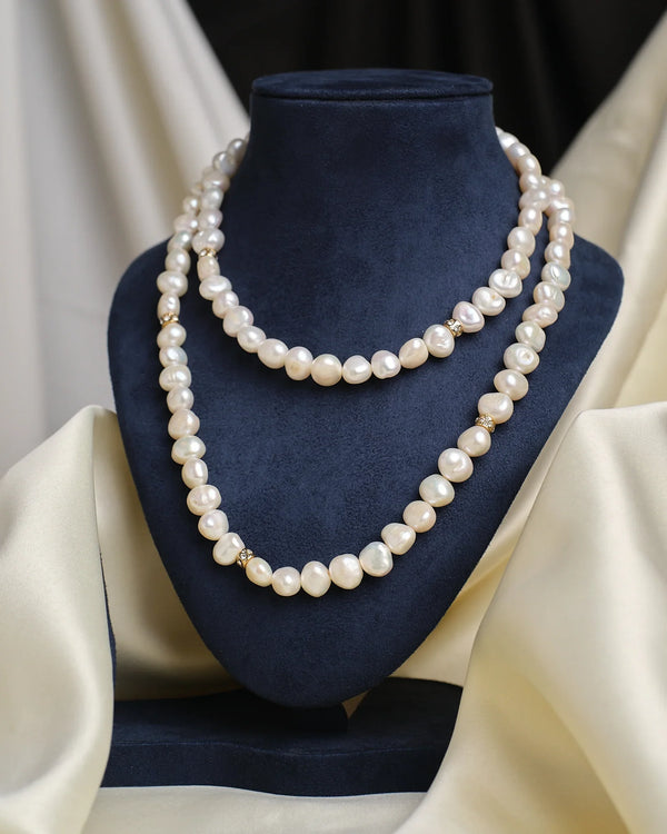 The Un-even Shaped Pearl Lariat with CZ Charm by Chandrani Pearls is showcased on a dark blue velvet bust with cream fabric accents—an elegant evening jewelry piece.