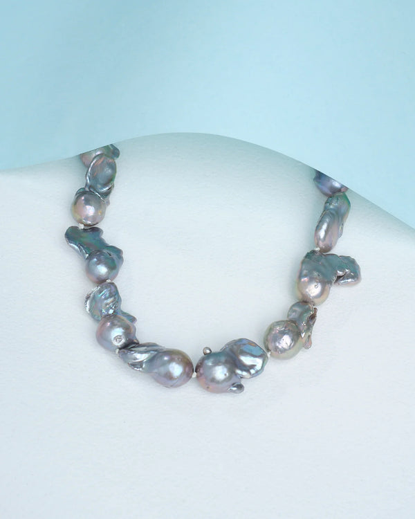 The "Timeless elegance in every pearl" necklace by Chandrani Pearls, featuring large baroque pearls, is partially veiled beneath a sheet of light blue paper.