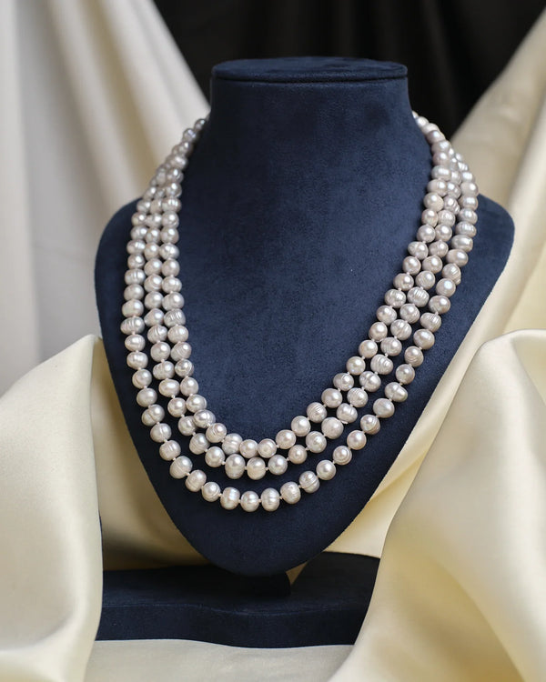 The Knotted Pearl Necklace by Chandrani Pearls is showcased on a dark blue velvet bust, with soft cream fabric elegantly draped in the background.