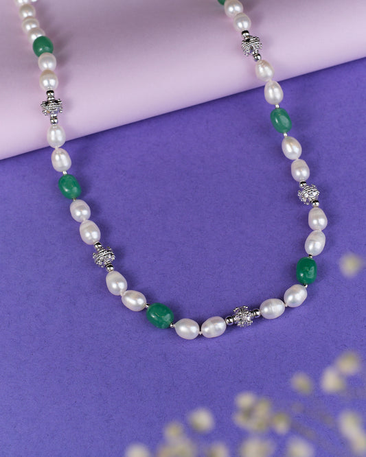 The Rasvatta - The Olive Elegance Pearls And Beads Necklace by Chandrani Pearls, showcasing alternating white pearls, green beads, and silver accents, elegantly rests on a purple surface with a pink edge.