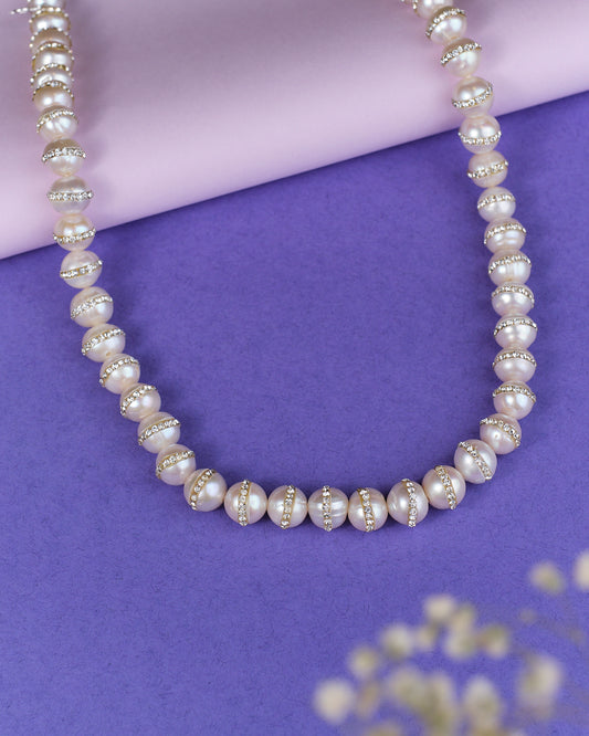 The Velakula-The Coastline Stories Pearl Necklace by Chandrani Pearls, featuring gold and crystal spacer beads, is elegantly showcased on a purple surface.