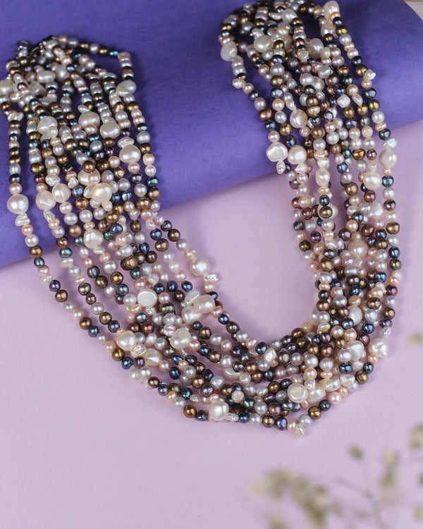 The Anuragini Multi Colour Pearl Necklace by Chandrani Pearls features luxurious strands of assorted freshwater pearls in various hues, elegantly displayed on a purple and pink background.