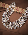 The Chandrani Pearls Fashion Multicolor 10 Line Pearl Mala, featuring white, pink, and lavender pearls, is displayed on brown fabric with a decorative ribbon—an elegant choice for wedding jewelry.