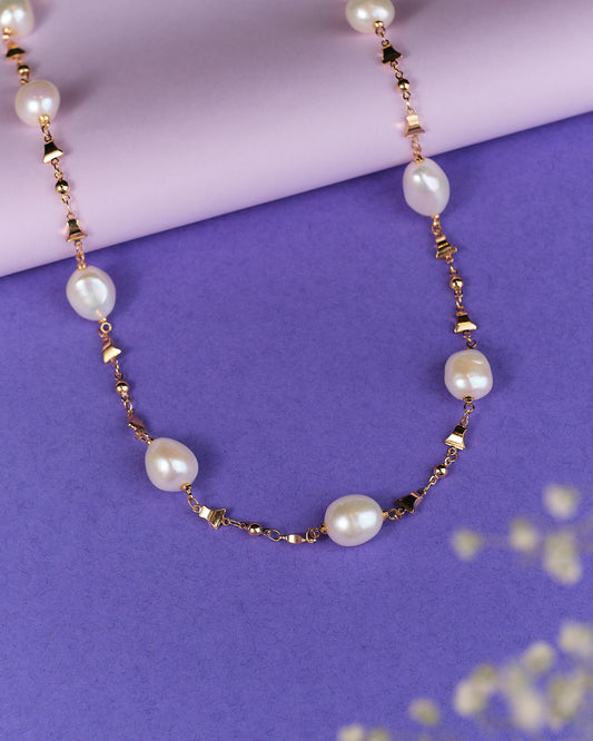 The Infinite Grace-Golden Statement Pearl Necklace by Chandrani Pearls exudes elegance, beautifully displayed on a purple surface with a lavender background, capturing the essence of luxury.