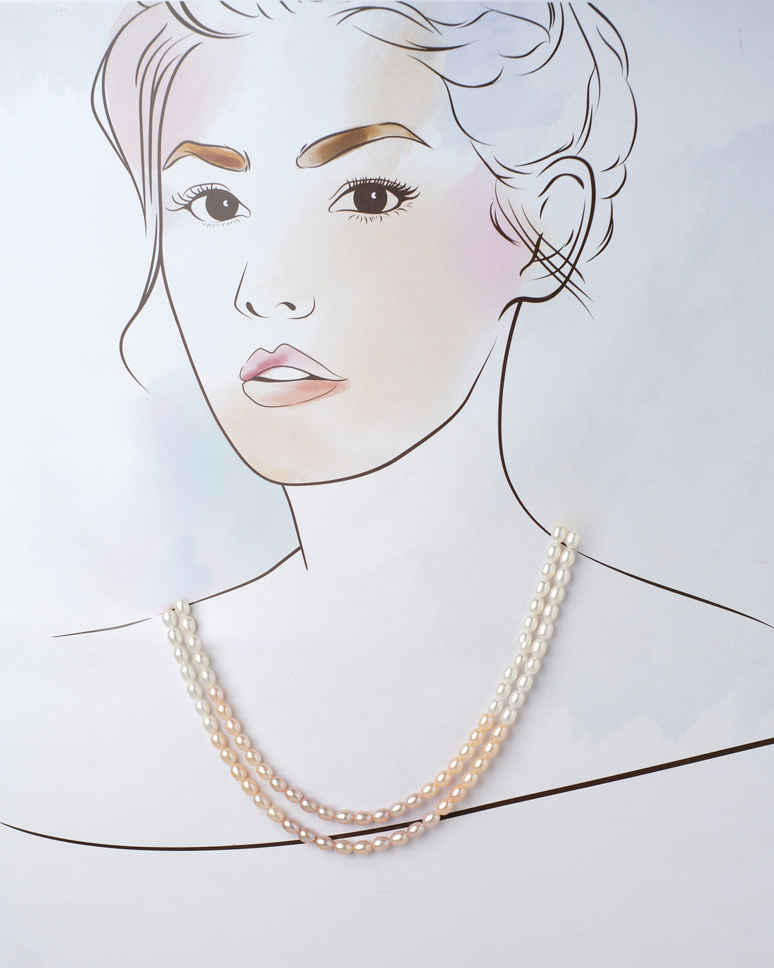 The Bhadrashochi Pearl Necklace by Chandrani Pearls features two luxurious strands, one white and one peach, elegantly arranged on a purple roll atop a pink surface adorned with small corner flowers.
