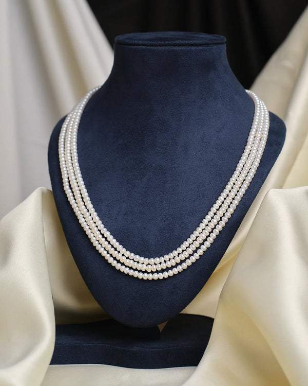 A sophisticated display showcases the Chandrani Pearls Classic White Pearl Necklace on a dark blue velvet bust, set against cream fabric in the background.