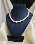 The Classic Elegance Pearl Necklace by Chandrani Pearls is showcased on a blue velvet bust with cream draped fabric, highlighting its timeless beauty—an exquisite pearl jewelry piece for any occasion.