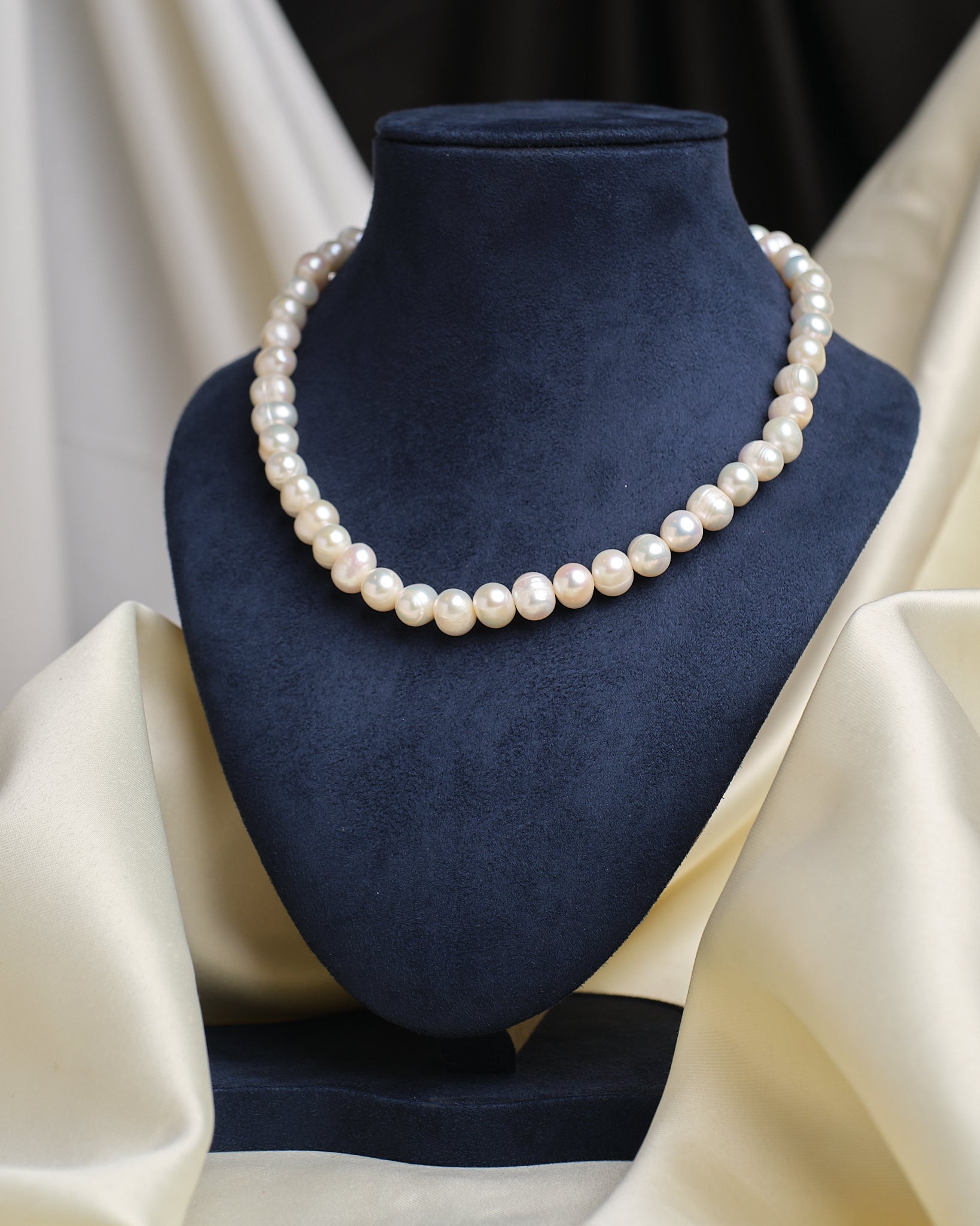 The Classic Elegance Pearl Necklace by Chandrani Pearls is showcased on a blue velvet bust with cream draped fabric, highlighting its timeless beauty—an exquisite pearl jewelry piece for any occasion.