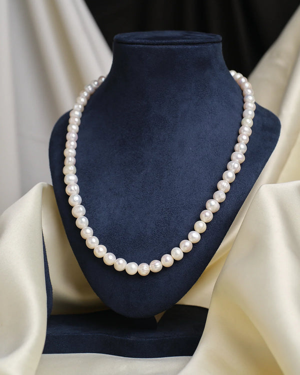 The Chandrani Pearls Layered Pearl Necklace is shown on a dark blue velvet bust with cream fabric in the background.