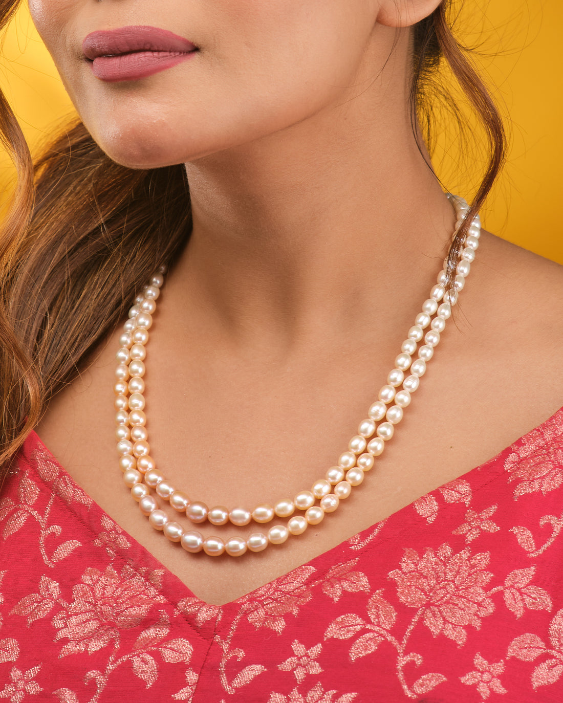 The Graduated Pearl Necklace by Chandrani Pearls, a classic double-stranded design, is displayed on a dark blue velvet bust with cream fabric draped in the background.