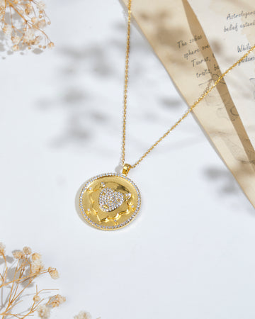 Displayed on a white surface alongside dried flowers and partially visible pieces of paper with text is the stunning Soul Of The Lion Leo Pendant by Chandrani Pearls. This gold pendant necklace, adorned with a floral design and encrusted with diamonds, perfectly embodies the elegance and strength symbolized by the lion.