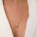 The Undying Love Pendant by Chandrani Pearls, a gold necklace with a diamond-studded infinity symbol, worn over a white blazer, perfectly captures everlasting love and timeless elegance.