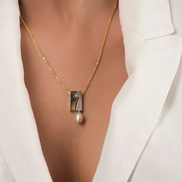 Wearing the Selene Pearl Pendant by Chandrani Pearls—a gold necklace with a rectangular wavy design and hanging pearl—paired with a white blazer, exudes timeless elegance.
