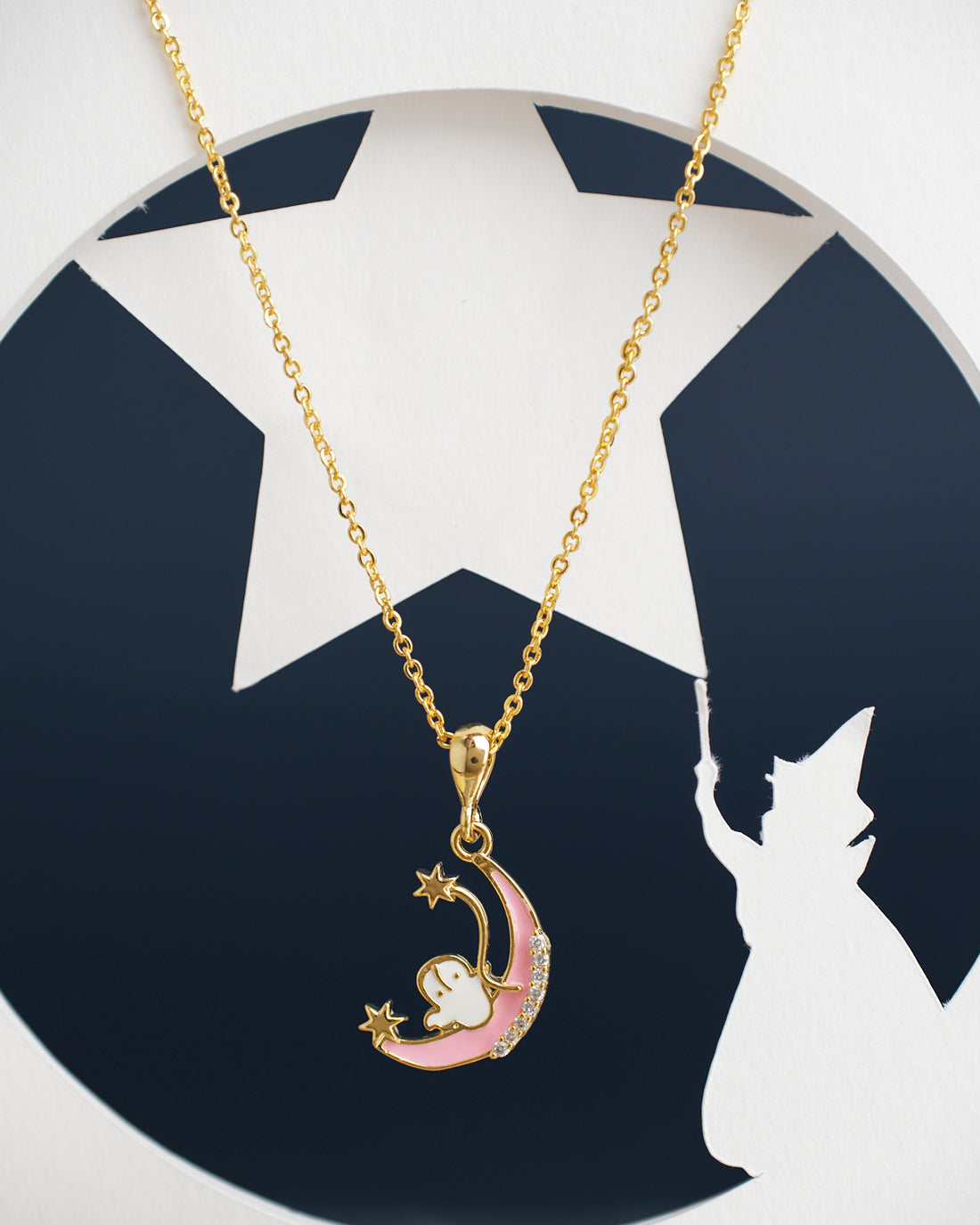 The Half Moon Cute Pendant by Chandrani Pearls India is a gold necklace featuring a crescent moon and stars design, set against a backdrop with a silhouette of a figure holding a wand in front of a starry sky.