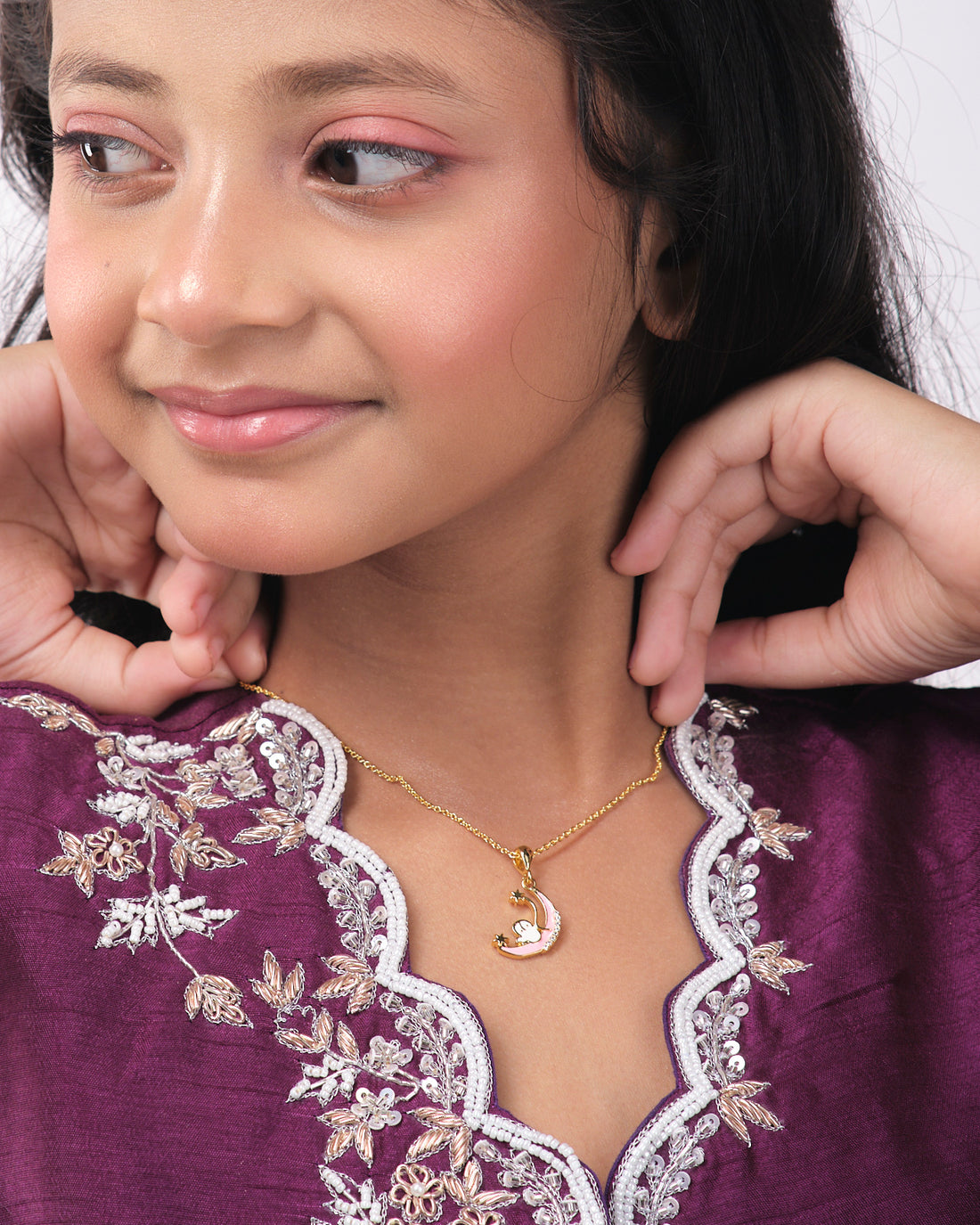The Half Moon Cute Pendant by Chandrani Pearls India is a gold necklace featuring a crescent moon and stars design, set against a backdrop with a silhouette of a figure holding a wand in front of a starry sky.