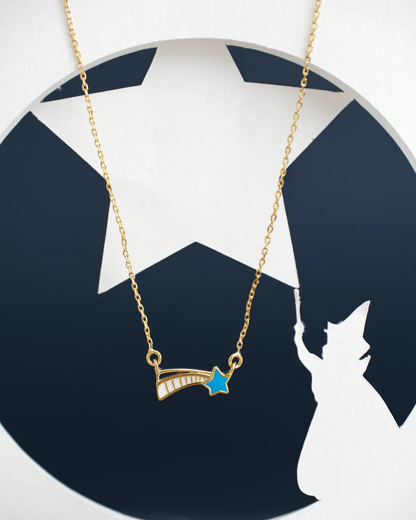 The Little Star Beautiful Pendant by Chandrani Pearls India, a gold necklace with a shooting star charm, is set against a backdrop featuring a star cutout and the silhouette of a figure holding a wand.