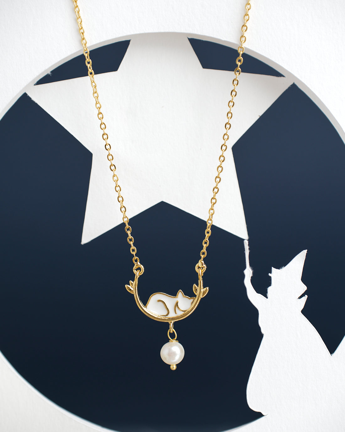 The Sleepy Cat Pretty Pendant by Chandrani Pearls India, featuring a gold finish with a fox and pearl design, is showcased against a backdrop highlighting a wizard's silhouette and star.