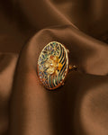 An elegant, iridescent ring by Chandrani Pearls dazzles with mother-of-pearl beauty, floral accents, and geometric design, showcased on rich brown satin fabric.