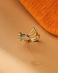 The Trendy Beautiful Ring by Chandrani Pearls, featuring a gold polish, fan-shaped bow design, and central square CZ stone, is displayed on a beige surface beside orange textured fabric.