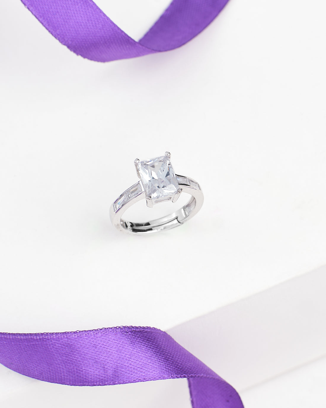 Chandrani Pearls' Classic Demifine Silver Ring with Romantic CZ Center is shown on a white surface, highlighted by a nearby purple satin ribbon.