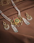 The Heritage Royal Pearl Set by Chandrani Pearls, featuring a gold, green, and pearl necklace with matching earrings, is displayed on a brown fabric background.