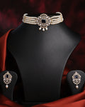 The Newfangled Pearl Necklace Set by Chandrani Pearls, featuring white pearls and gold disc accents with matching earrings, is showcased on a black jewelry stand against a dark red background.