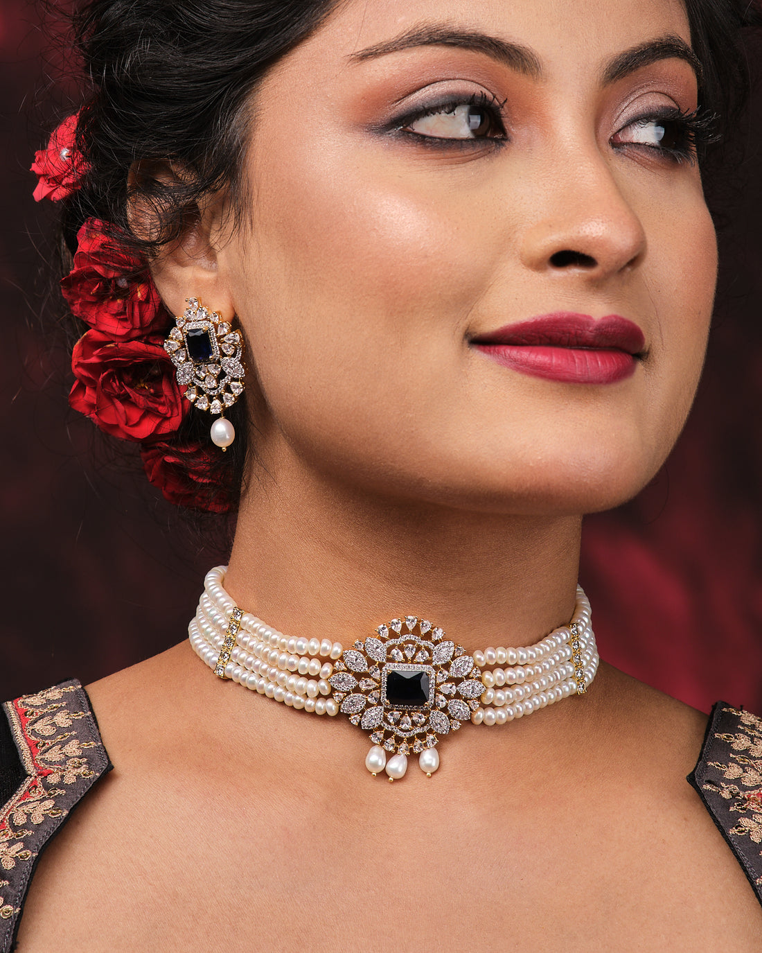 The Newfangled Pearl Necklace Set by Chandrani Pearls, featuring white pearls and gold disc accents with matching earrings, is showcased on a black jewelry stand against a dark red background.