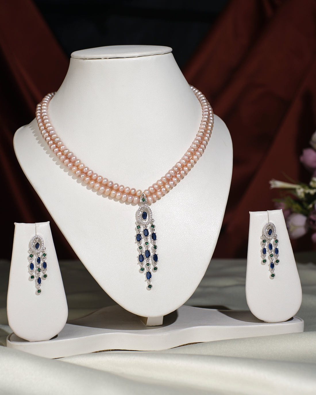 The Chandrani Pearls India Trendy Pearl Necklace Set, featuring a jeweled pendant and matching drop earrings, displayed on white stands against a draped backdrop—the ideal upgrade for your jewelry collection.