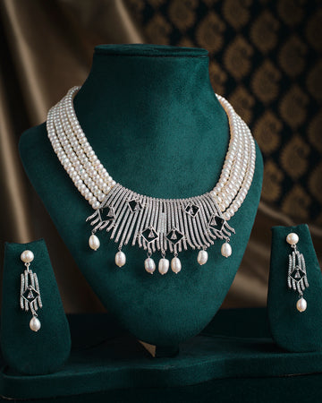 The Rang Tarangini Pearl Necklace Set by Chandrani Pearls, featuring teardrop and geometric details, is elegantly displayed with matching earrings on a green velvet stand.